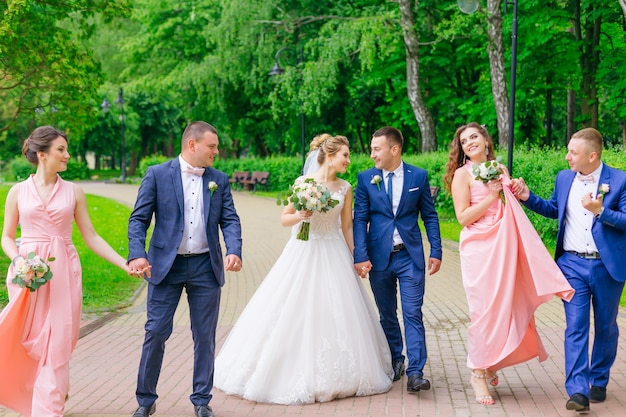 Newlyweds and their friends hold hands and walk in the park.