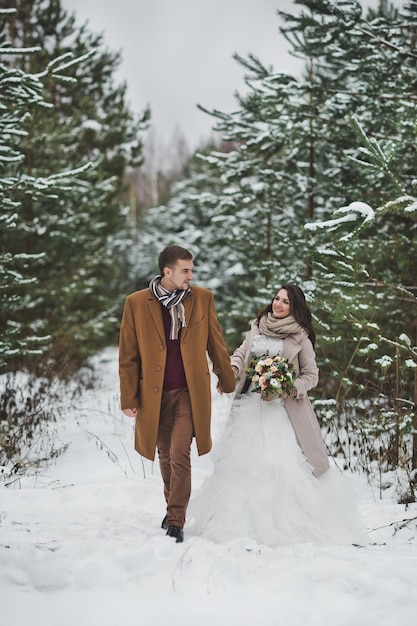 Photo newlyweds walk among snowcovered trees and pines 840