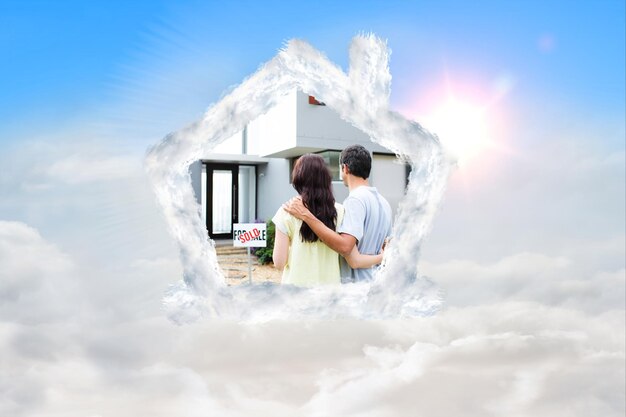 Newlyweds with their new house against blue sky with white clouds