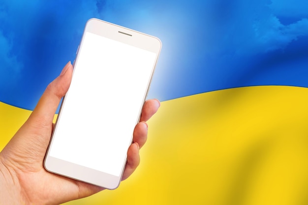 전화로 우크라이나 뉴스 채널 한 여성의 손이 우크라이나 국기 배경에 빈 화면이 있는 휴대전화를 들고 있다