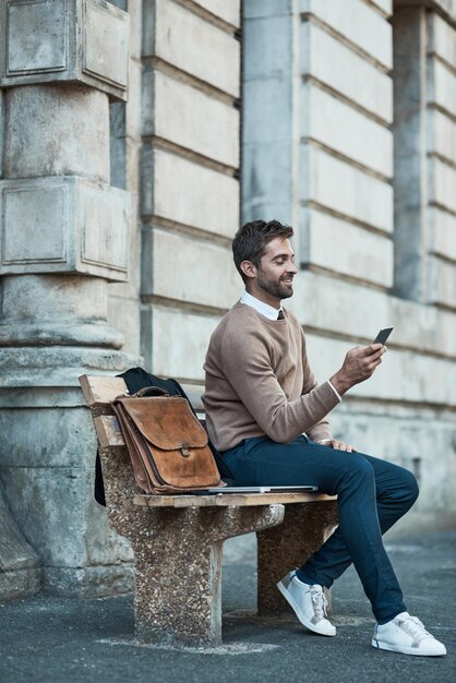 The news Ive been waiting for Full length shot of a handsome businessman using his cellphone while sitting on a bench in town