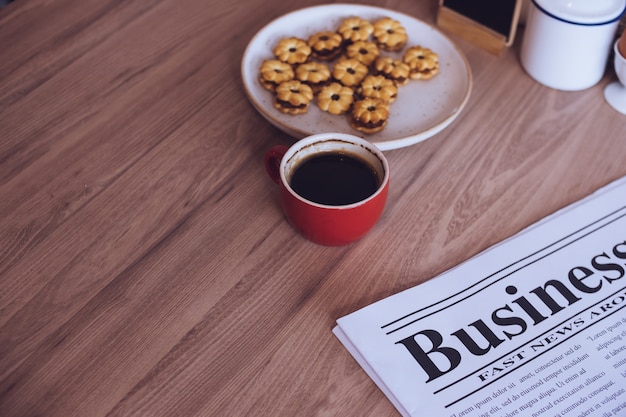 Newspaper, a cup of coffee and snacks on a wooden table.