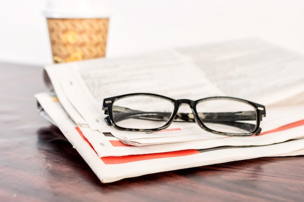 Newspaper and reading glasses on wooden table