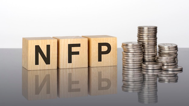 NFP text on wooden cubes on a cold grey light background with stacks coins