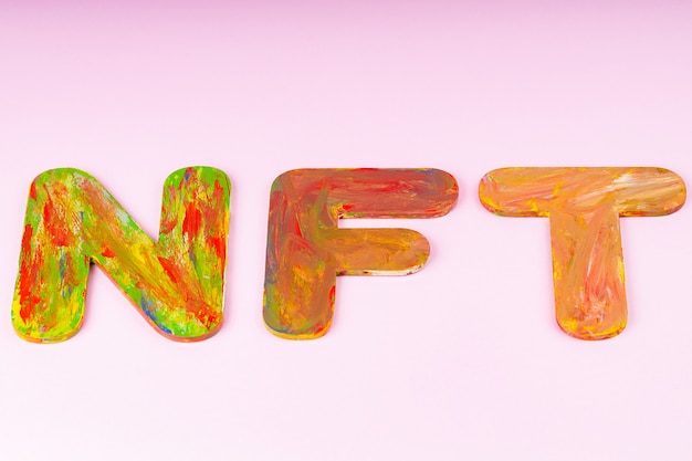 NFT-inscriptie op roze achtergrond. Niet-fungible token samengesteld uit veelkleurige letters, bovenaanzicht. Crypto kunst concept