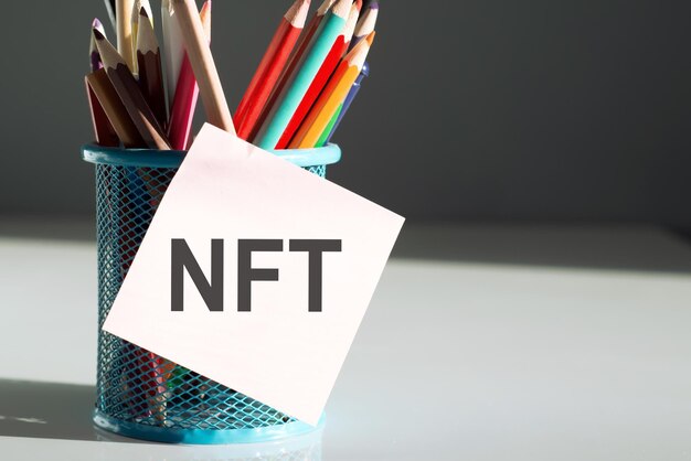 Текст NFT на липкой чашке с разноцветными карандашами