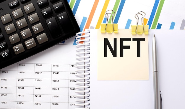 NFT text, written on a sticker with calculator,pen on the chart background.