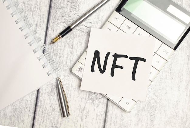 NFT text written on a sticker with calculator on wooden background