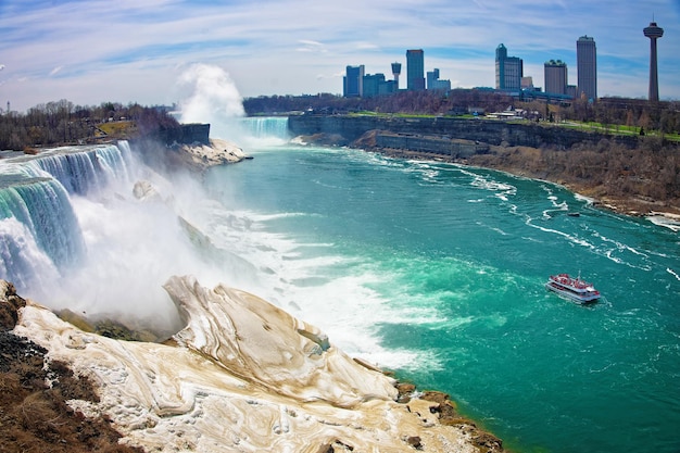 Niagara Falls and Ferry on Niagara River from the American side. A view on American Falls, Bridal Veil Falls, Goat Island, Horseshoe falls and Canada Skyscrapers on the background.