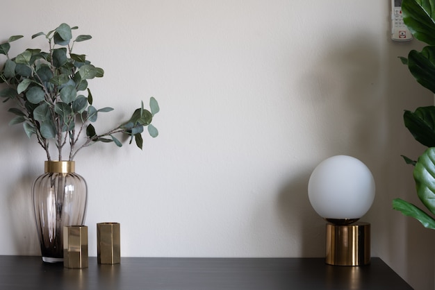 Bella pianta artificiale in vaso di vetro con bordo in acciaio inossidabile dorato e vaso a specchio dorato e lampada posizionata su un tavolo di legno nero vuoto.
