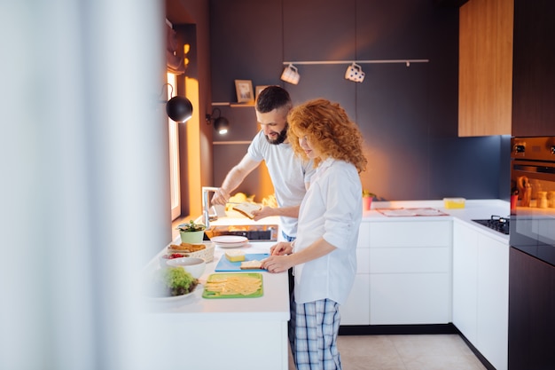 Nice bearded man helping his wife to make a sandwich