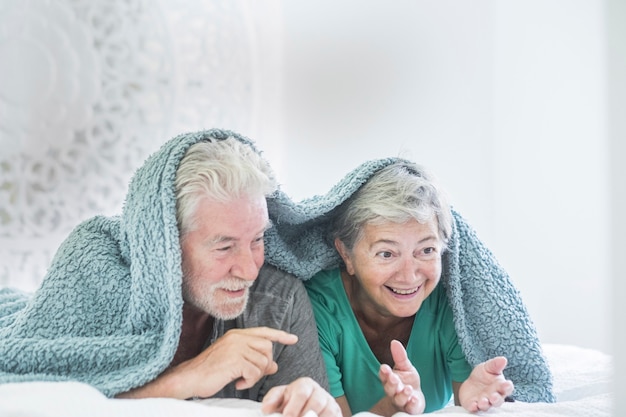 Nice and beautiful cheerful couple of retired adult senior couple play together under the blanket at home