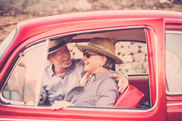 Bella bella coppia di persone adulte anziane all'interno di una vecchia auto d'epoca rossa divertirsi e stare insieme in attività di viaggio all'aperto. sposati e per sempre insieme la vita. concetto di viaggio con felicità