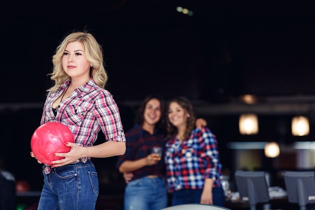 Хорошая блондинка девушка с шаром для боулинга, подруги в фоновом режиме