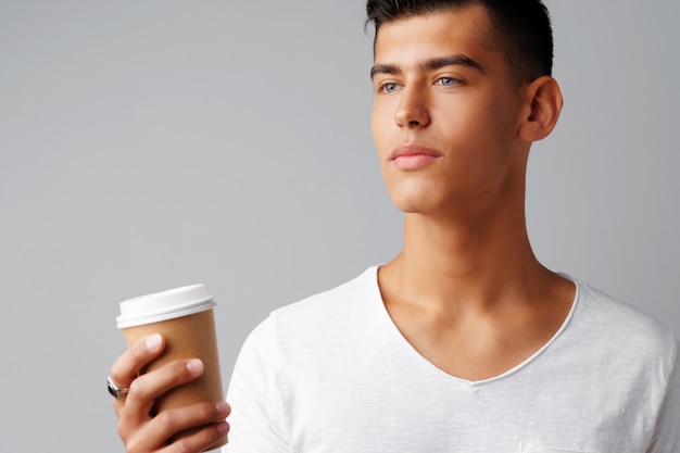 Nice brunette young man holding a cup of coffee over a gray background