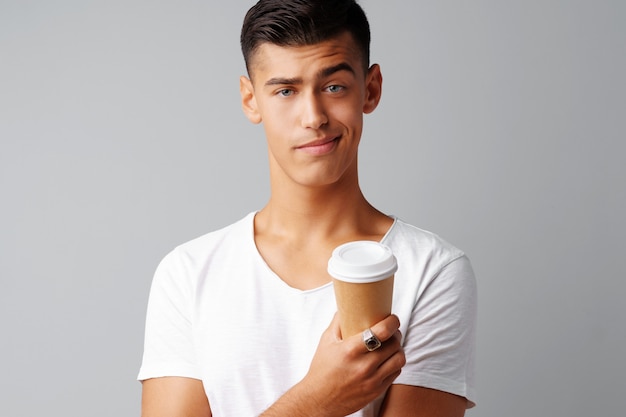 Nice brunette young man holding a cup of coffee over a gray background