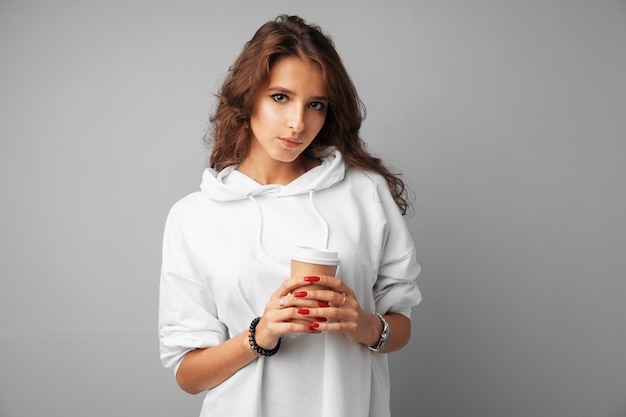 Giovane donna piacevole del brunette che tiene una tazza di caffè sopra un gray