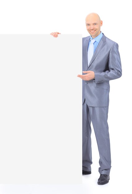 Nice businessman holds white poster. Isolated on a white wall.