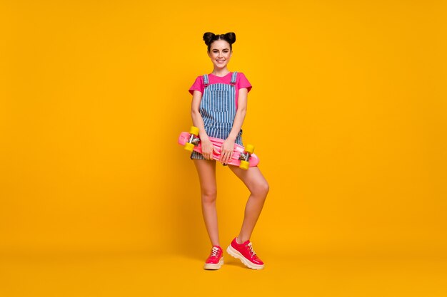 Nice cheery girl holding skate board on yellow color background