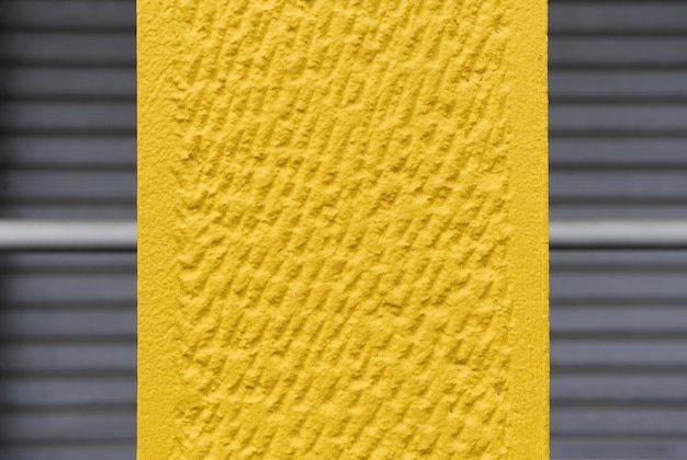 Nice concrete background toned yellow against closed gray\
shutters wall surface texture grunge bright illuminating color\
background in gray urban context yellow and gray colors of the\
year