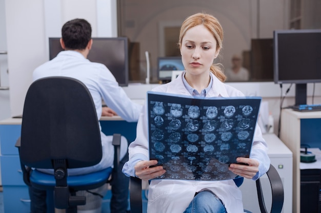 Nice cute female doctor holding an X ray image and examining it while putting a diagnosis