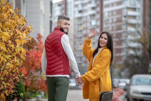 Nice dark haired woman greeting you on the street while walking with her boyfriend