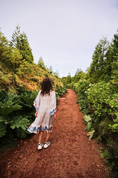 Foto bella vista posteriore di una giovane donna in abito bianco che cammina lungo un bellissimo vicolo con