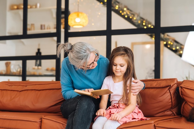 Nice elderly woman grandmother reading story to granddaughter. Happy family at home concept