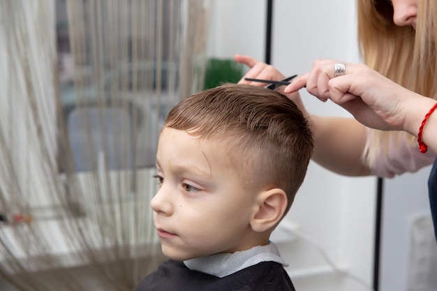 Nice european little boy getting hairstyle in barbershop