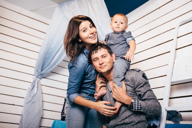 屋内の明るいモダンなインテリアのスタジオの背景にある素敵な家族。一緒にポーズをとる子息子と若い母と父の笑顔。