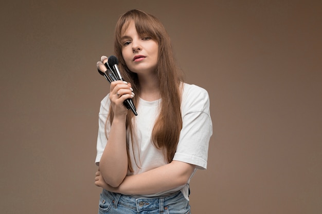 Nice girl holds makeup brushes on dark brown