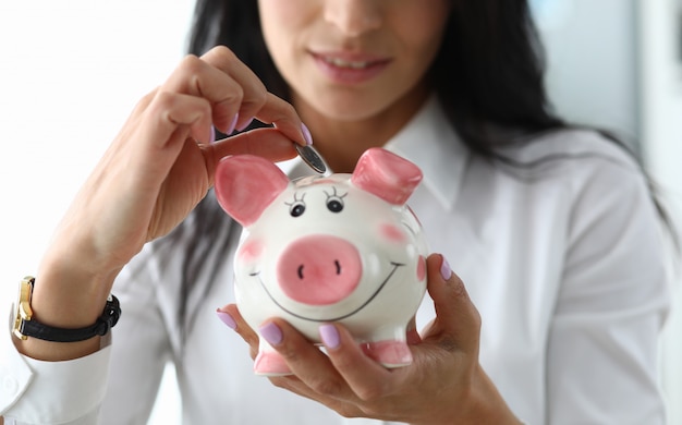 Nice girl puts a coin in ceramic pig figurine