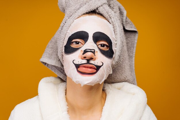 Nice girl with a towel on her head and in a bathrobe after a shower on her face a moisturizing mask with a panda face