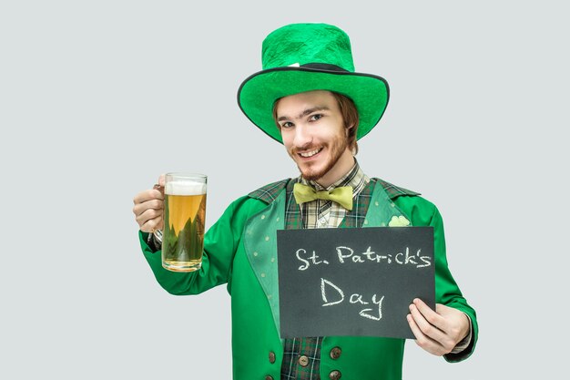 Nice happy young redhead man holding mug of beer and dark plate in hands. He look  and smile. It's saint patrick's day. Isolated on grey .