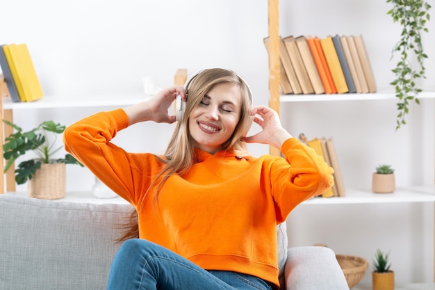 Nice joyful girl listening music with headphones and cellphone while sitting on couch at home