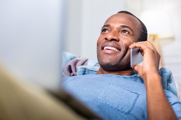 Nice joyful positive man smiling and holing his smartphone while having a phone conversation