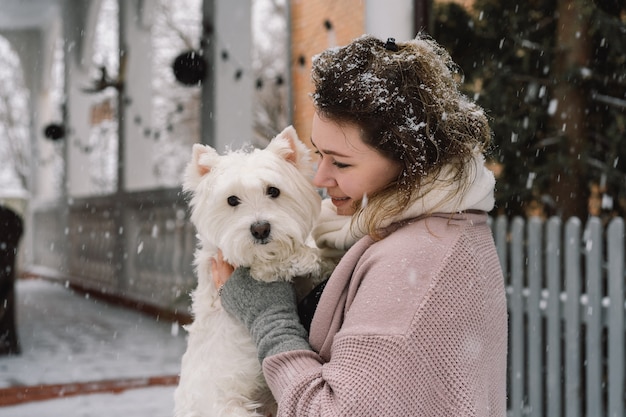 Nice laughing girl hugging adorable white dog with funny cute emotions. West highland white terrier. Adoption concept.