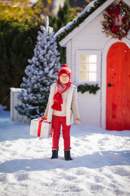 赤い帽子と緑色の眼鏡の素敵な小さな男の子がクリスマスツリーの近くに大きなプレゼントを見つける