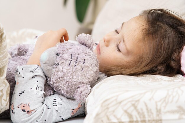 Nice little dark haired girl sleep stroke and embracing the\
best furry friend bear toy in bed calm deep sleep at home