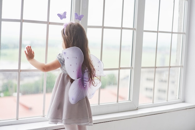 Bella bambina vestita da fiaba in piedi vicino alle finestre e guardando fuori.