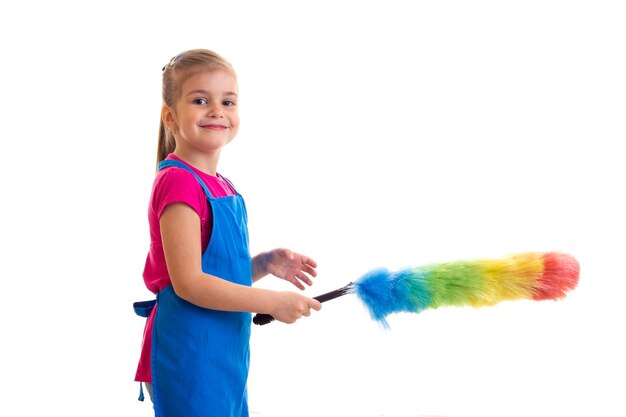 Nice little girl with ponytail wearing in pink shirt and blue apron with colored duster in studio