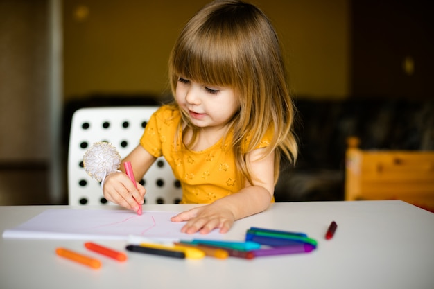 Nice little girl in the yellow dress drawing with wax pastel