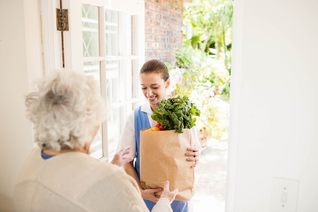 Foto bella infermiera che porta le verdure al paziente anziano a casa