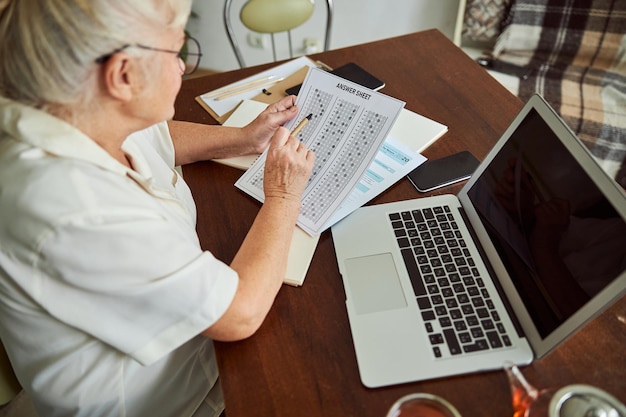 Photo nice old woman checking answers for test and using laptop