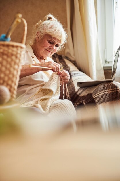 Photo nice old woman knitting and using notebook at home