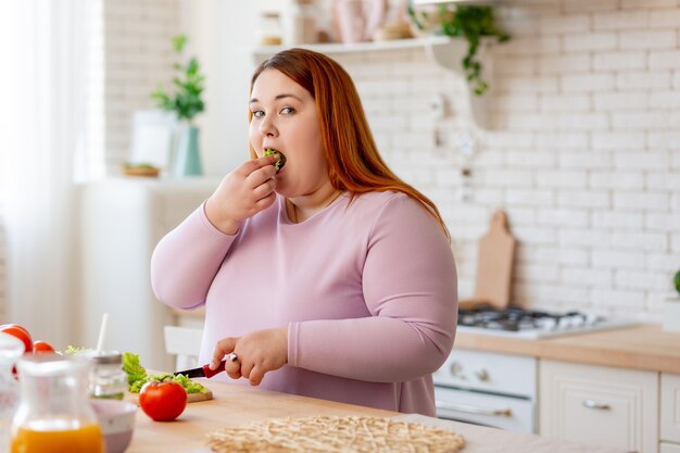 Bella donna sovrappeso che mangia foglie di lattuga verde mentre si sente molto affamata