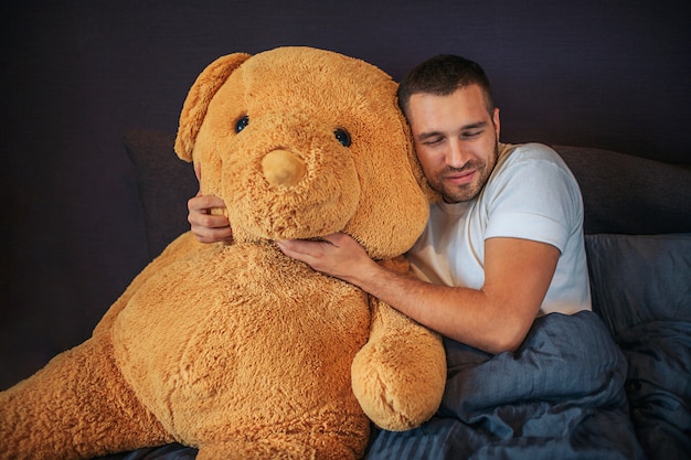 Красивое изображение взрослого с большой игрушкой оранжевого медведя. Парень обнимает и наклоняется к нему. Он держит глаза закрытыми. Человек отдыхает. Он болен.