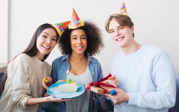 Nice picture of a birthday girl and her friends. Asian girl has a piece of cake. The guy holds a present in his hands. All of them are happy.