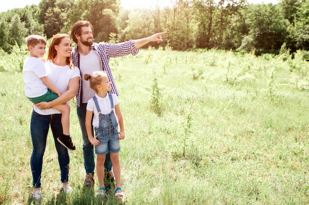 Nice picture of family standing together on meadow. Mom is holding her son on hands. Girl is standing besides her parents. Guy is pointing down further.