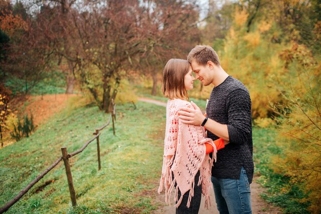 Nice picture of young and happy man and woman. They stand on meadow close to each other. He holds his hands on her shoulders.